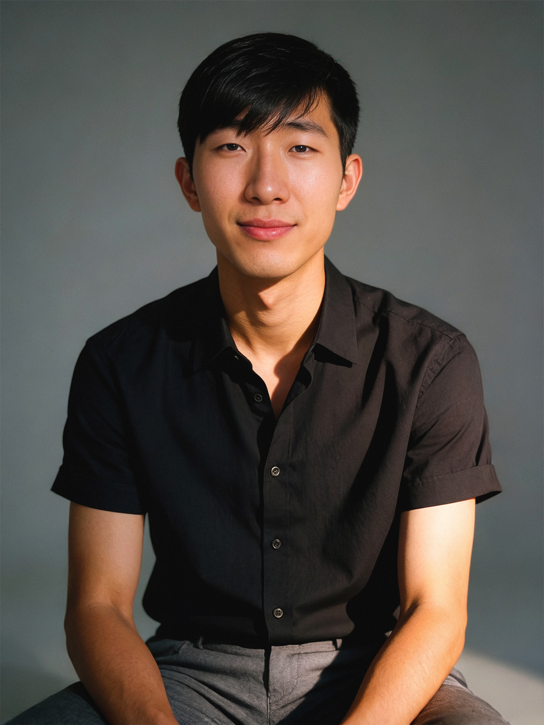 a smiling, handsome dark-haired person poses for a portrait in a black t-shirt