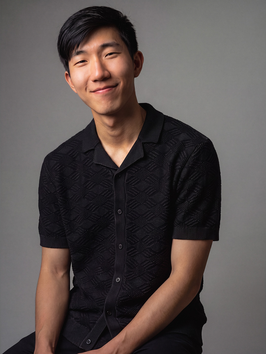 a smiling, handsome dark-haired person poses for a portrait in a black t-shirt